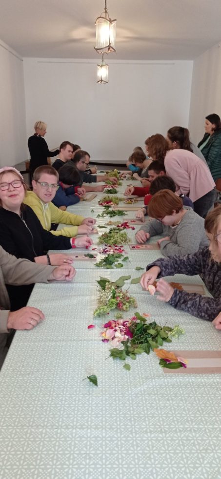 Grupa uczniów przy długim stole wykonują prace plastyczne z suszonych roślin.