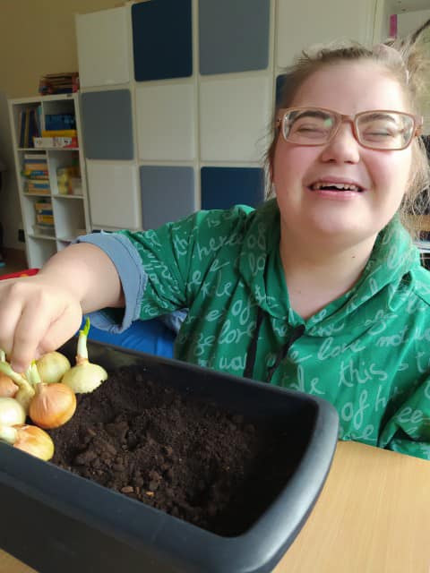 Na zdjęciu Agatka sadzi cebulkę do doniczki z ziemią.