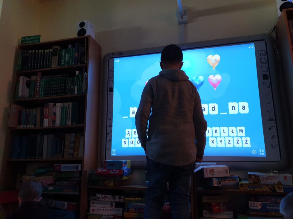 Chłopiec rozwiązuje krzyżówkę słowną na dużym monitorze.