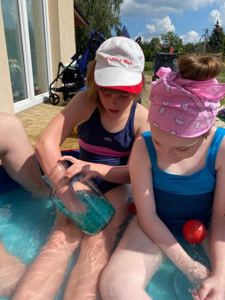 Na fotografii dwie dziewczynki siedzą w basenie i bawią się wodnymi kulkami.