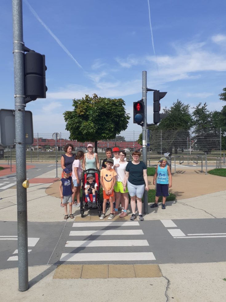 Na fotografii uczniowie wraz z opiekunem w drogowym miasteczku. stoją na czerwonym świetle przed pasami dla pieszych.