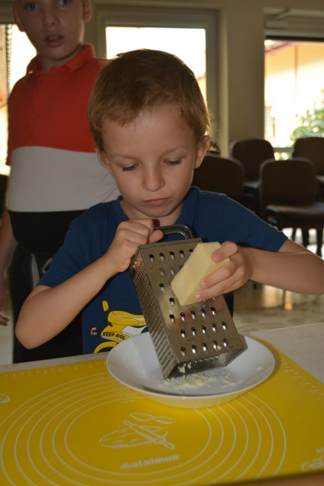 Na zdjęciu Natan trze żółty ser na tarce.
