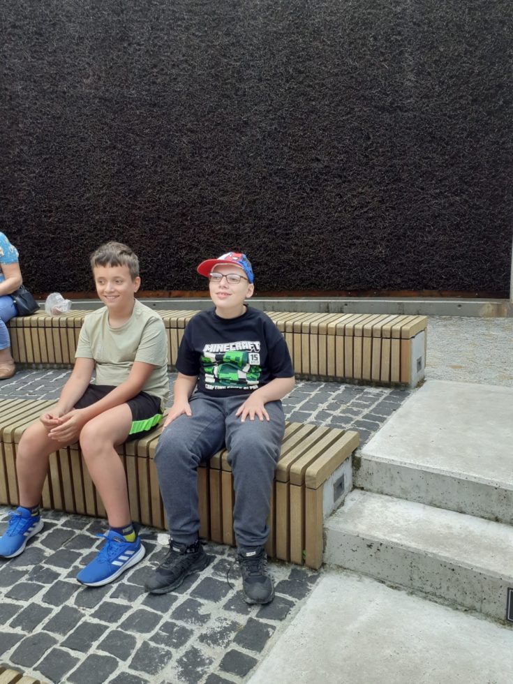 Na fotografii dwaj chłopcy siedzą na ławce przy tężni solankowej.