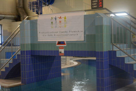 Na zdjęciu kawałek basenu w Krytej pływalni oraz baner z napisem Międzyośrodkowe Zawody Pływackie dla Osób Niepełnosprawnych.