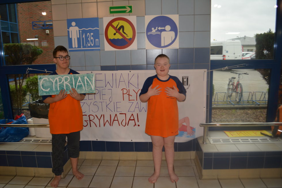Na zdjęciu Grzegorz trzyma napis Cyprian, obok stoi Cyprian uczestnik zawodów pływackich, zdjęcie w strefie kibica.