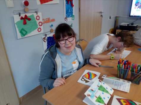Na obrazku znajduje sie uśmiechnięta Emilia, obok niej Wiktoria wypisuje kartkę świąteczną
