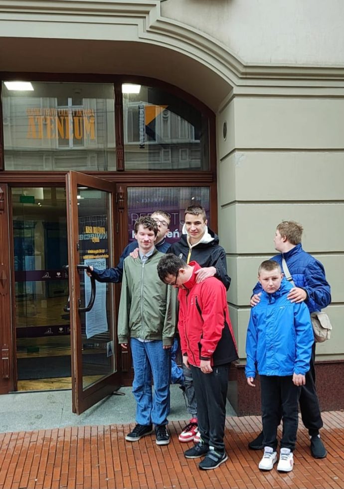 Na fotografii chłopcy stojący u drzwi teatru, jeden z nich trzyma otwarte drzwi.