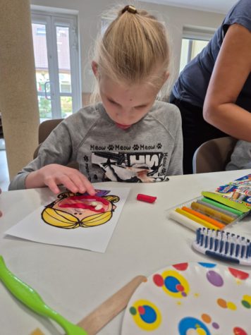 Na zdjęciu dziewczynka siedzi przy stole, przykleja białe fasolki do plasteliny, które imitują zęby.