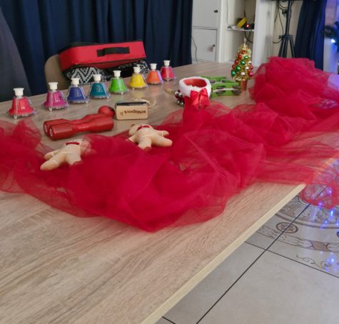 Na zdjęciu widać stół, na stole leżą instrumenty muzyczne, kolorowe dzwonki, grzechotki, tamburyn oraz atrybuty świąteczne, pluszowe ciasteczka, choinka i buty świętego Mikołaja. Wszystko otoczone jest czerwonym tiulem.