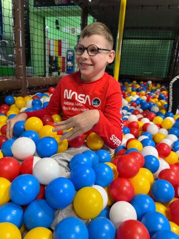 Na zdjęciu chłopiec w okularach siedzi w kolorowych piłkach.