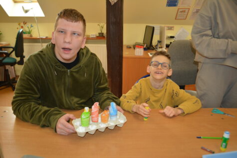 Na zdjęciu dwaj chłopcy siedzą przy stole, mniejszy ma okulary. Przed sobą maja wytłaczankę na jajka, gdzie powkładane sa postaci czterech pór roku. W tle biurko z monitorem i okno dachowe.