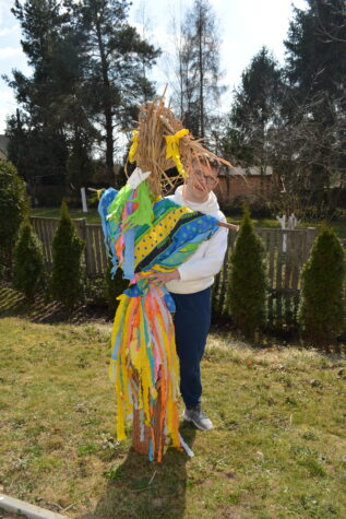 Na zdjęciu chłopak w okularach stoi na trawie obok wielka kukła przedstawiająca Marzannę.