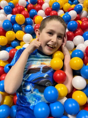 Na zdjęciu chłopiec leży w kolorowych plastikowych piłkach, wystaje z piłek głowa i ręce.