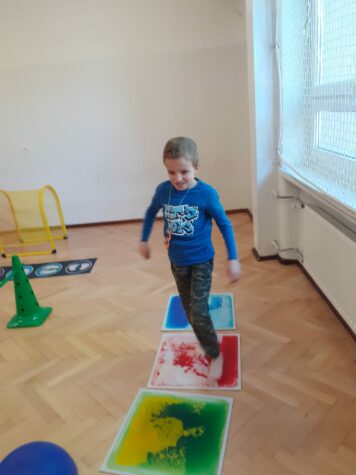 Na zdjęciu mały chłopiec idzie po planszach w kolorze niebieskim, czerwonym i zielonym.