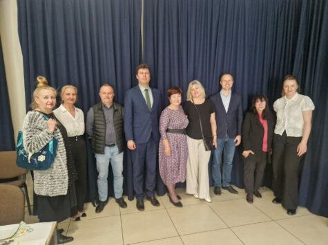Na zdjęciu stoją kobiety i mężczyźni. W tle granatowa kotara.