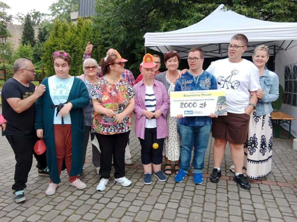 Na zdjęciu chłopcy i dziewczyny, uczestnicy Świetlicy Terapeutycznej oraz dwie kobiety. Jeden z chłopców trzyma duży symboliczny czek.