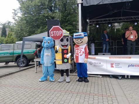 Na zdjęciu trzy duże maskotki stoją przed sceną. Niebieski smok, sygnalizacja świetlna trzyma w prawej ręce znak stop i chłopek w czapce z napisem Ratuś.