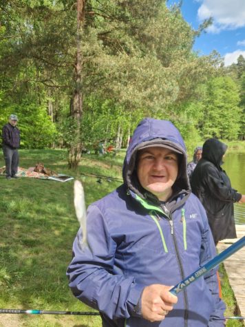 Na zdjęciu chłopak w kurtce z kapturem trzyma wędkę a na niej ryba podczas konkursu wędkarskiego.