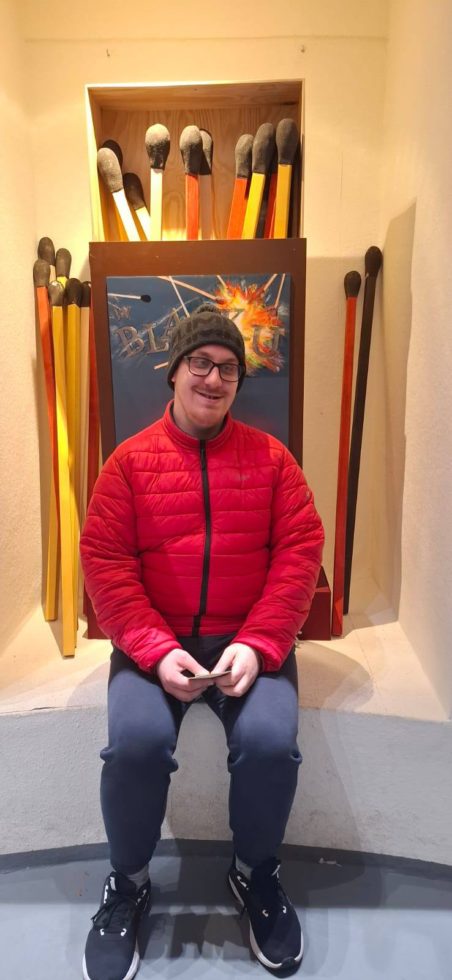 Na zdjęciu mężczyzna uczestnik Świetlicy Terapeutycznej siedzi, w tle duże pudełko z którego wystają duże zapałki.