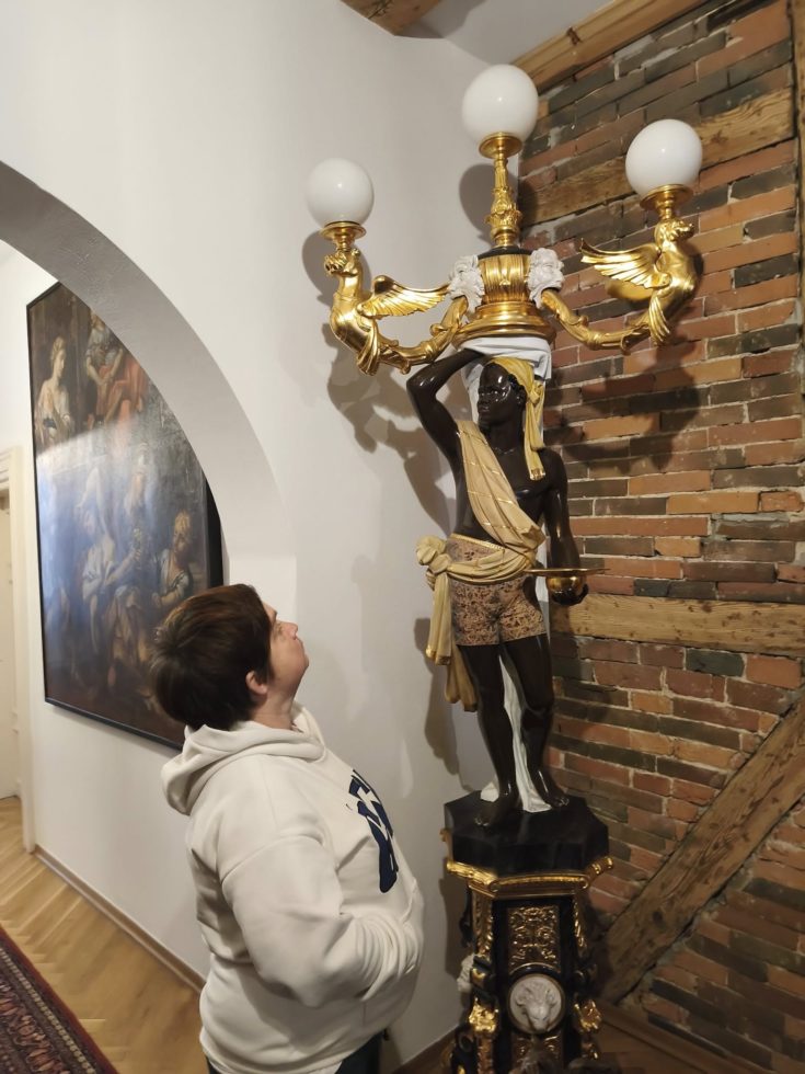 Na zdjęciu kobieta patrzy na figurę  ze zbiorów muzealnych , która jest lampą.