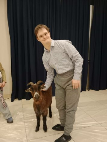 Na zdjęciu stoi mężczyzna, uczestnik Świetlicy Terapeutycznej, obok niego stoi prawdziwa koza. Mężczyzna głaska kozę.