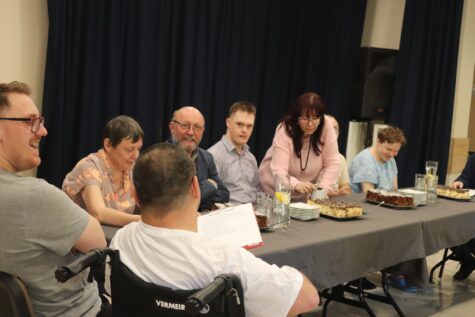 Na zdjęciu przy stole siedzą uczestnicy Świetlicy Terapeutycznej, mężczyźni i kobiety jeden na wózku inwalidzkim. Wśród nich zaproszony gość aktor Pan Artur Barciś.