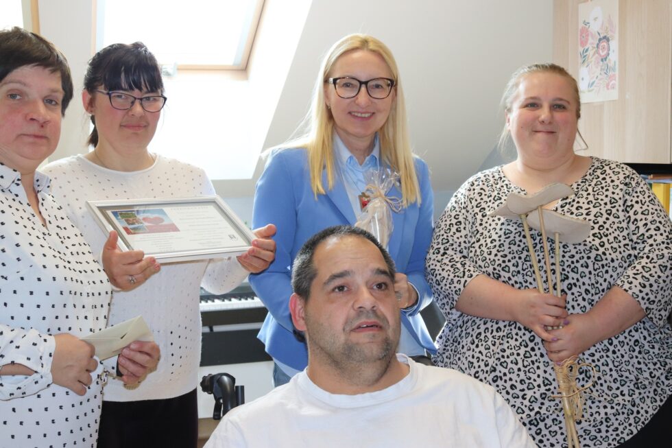 Na zdjęciu kobieta w okularach w niebieskiej marynarce, zaproszony gość trzyma ceramicznego anioła. Obok trzy kobiety i jeden mężczyzna uczestnicy Świetlicy Terapeutycznej, jedna kobiet trzyma ceramiczne kwiaty druga ramkę z podziękowaniami.