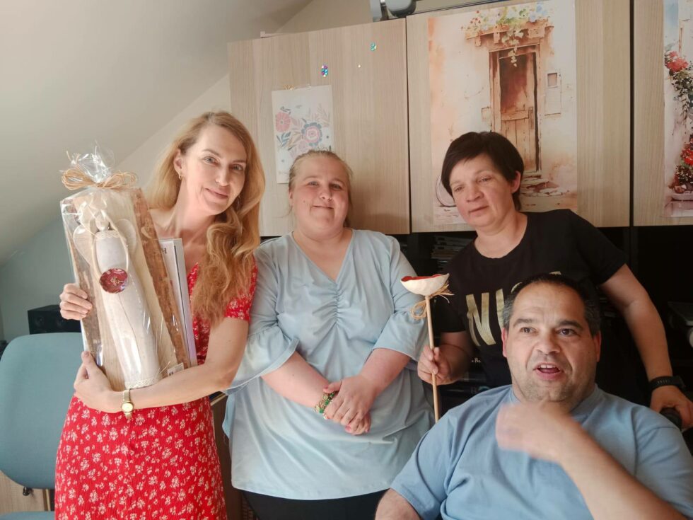 Na zdjęciu Pani Magdalena Waligórska  - Lisiecka aktorka wraz z uczestnikami Świetlicy Terapeutycznej. Dwie kobiety i mężczyzna. Pani Magdalena trzyma ceramicznego Anioła a jedna z kobiet ceramiczny kwiat na patyku.