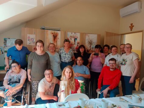 Na zdjęciu grupowe zdjęcie kobiety i mężczyźni uczestnicy Świetlicy Terapeutycznej wraz z opiekunami oraz zaproszony gość aktorka Pani Magdalena Waligórska - Lisiecka. W tle meble.