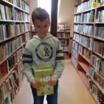 Na zdjęciu chłopiec z książką w bibliotece wśród regałów z książkami